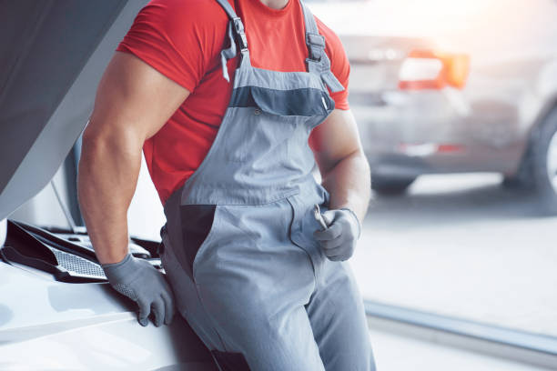 Handsome young auto mechanic in uniform is examining car in auto service.